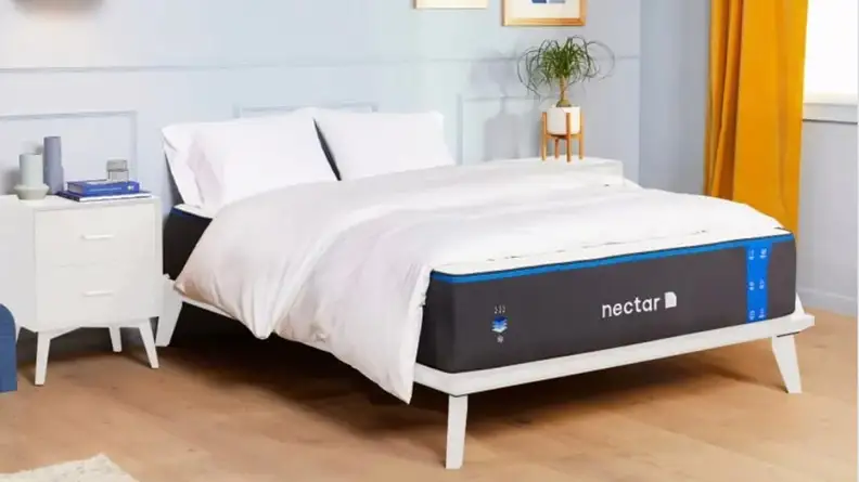 A Nectar mattress in a bedroom, covered with white bedding.
