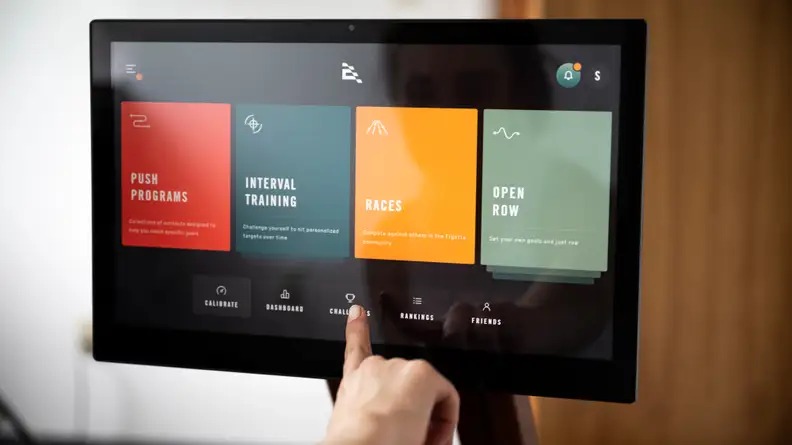 Hand pointing at Ergatta homescreen showing push programs, intervals, races, open row.