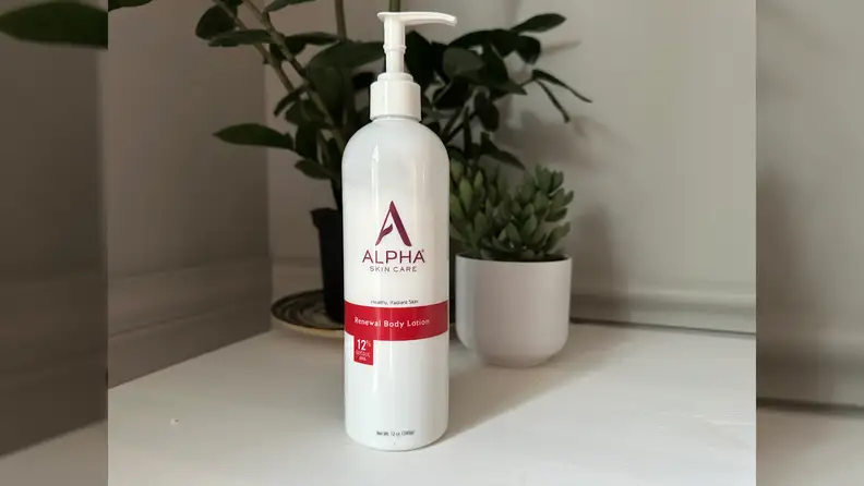 Alpha Renewal Body Lotion on a white floor in front of a plant.