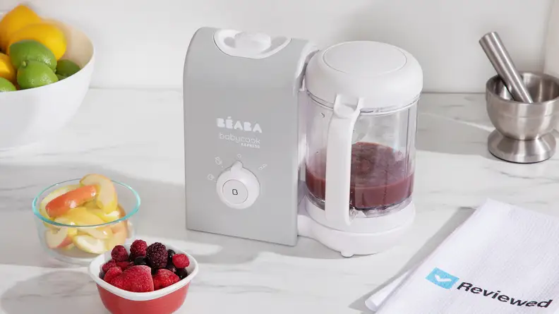 A Beaba Babycook Express sitting on a kitchen counter next to a bowl of berries.