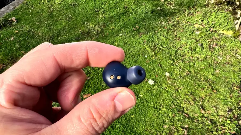 Person holding single Jabra Elite 4 Active headphone in-hand in front of grass.