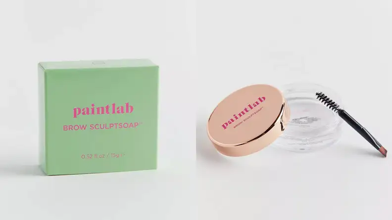 On the left: A small, light green box with pink lettering on it. On the right: A clear jar with clear brow gel in it uncapped with its gold lid and spoolie brush leaning on the jar.