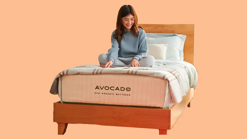 A woman sitting on an Avocado mattress against a peach background.