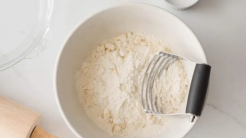 A dough blender lying in a bowl of pasta flour.