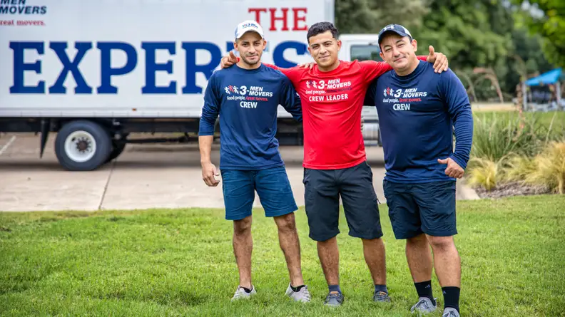 three men standing on a lawn in front of a moving truck