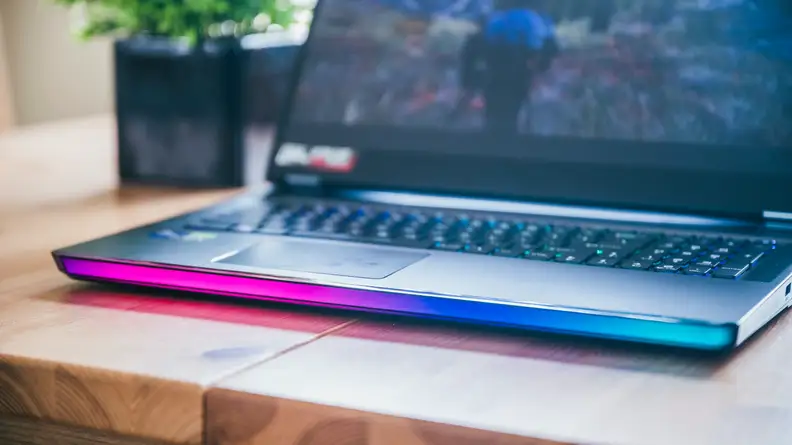 A laptop sitting on a desk with the camera focused on the colored lighting stripe around the front.