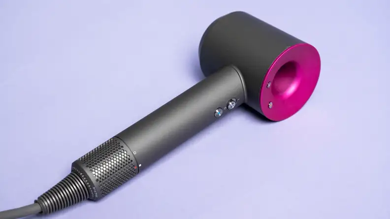 A charcoal gray and fuschia hair dryer laying on a light purple background.