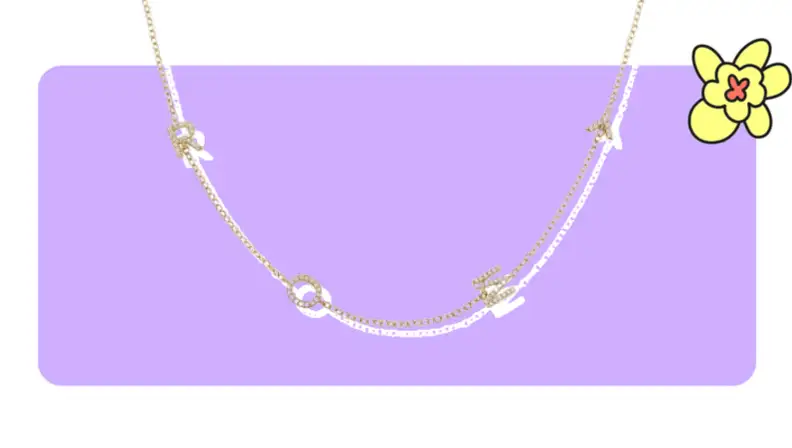 A gold pendant necklace with diamond-crusted letters in front of purple background with a yellow cartoon flower in the corner.