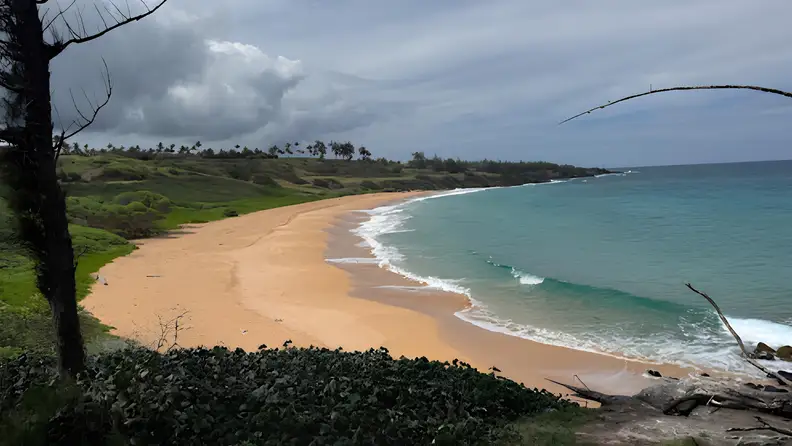Wide view of a quiet sandy beach with turquoise water and dramatic clouds overhead.