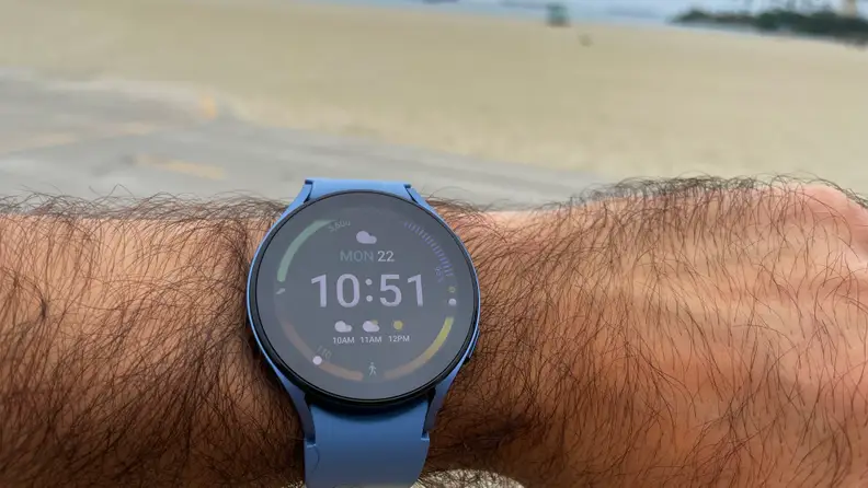 A powered-on smart watch with a light blue wristband wrapped around a person's wrist