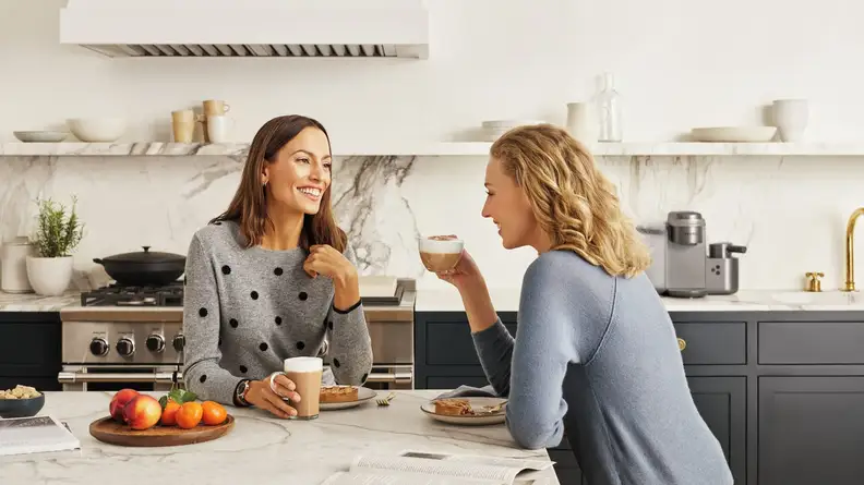 Two people enjoy coffee inside a kitchen.