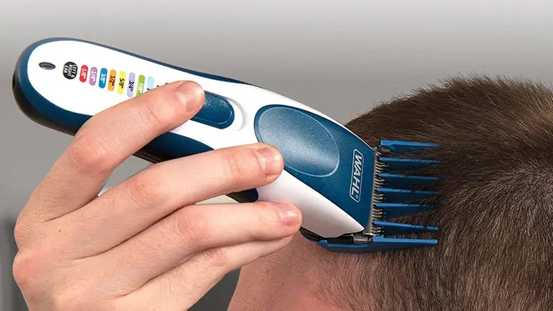 A person shaves their head with electric clippers.