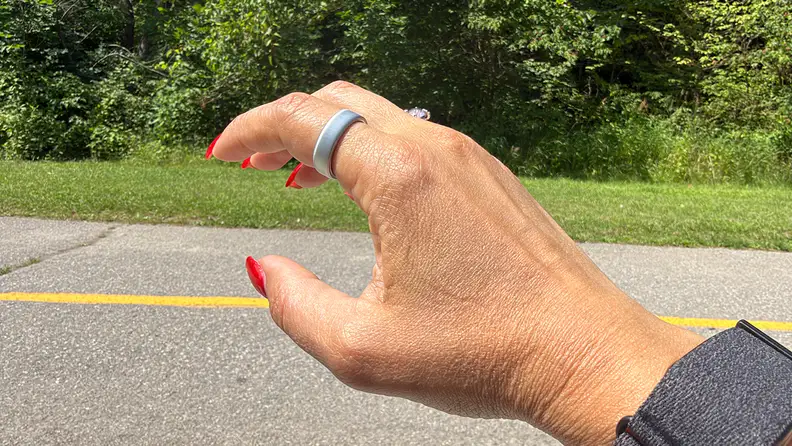 Right hand showing the Oura Ring 5 in front of a road with green grass behind it.