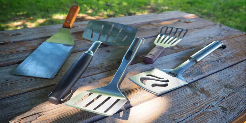 Five spatulas laid out on wooden surface outdoors