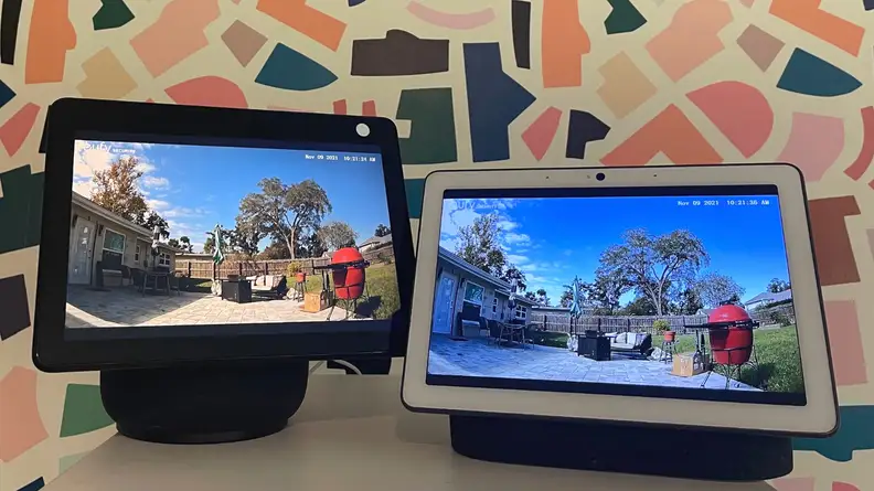Amazon Echo Show 10 and Google Nest Hub Max smart displays sit next to one another on a white table.