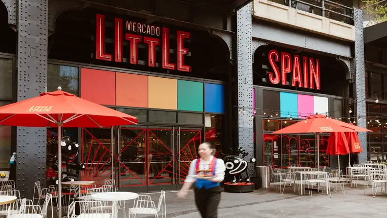 Entrance to Mercado Little Spain with red neon signage and umbrellas