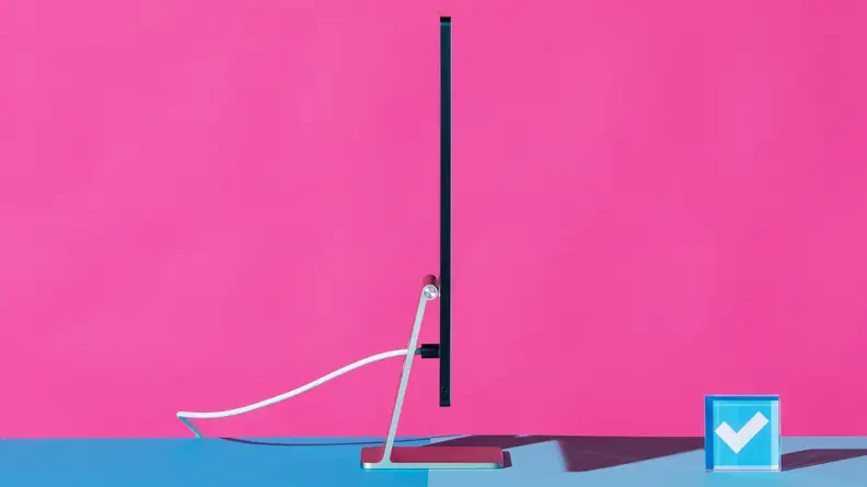 A profile view of an all-in-one iMac desktop computer standing on a blue surface against a hot pink background