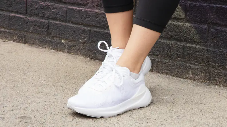 Person leaning on a brick wall outdoors while wearing a white pair of lululemon Beyondfeel sneakers.