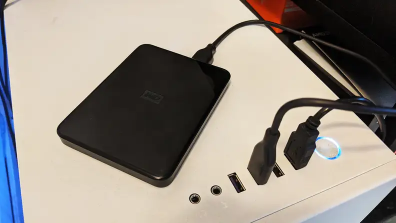 A small external hard drive plugged into the top of a desktop computer case backing files up for donation or recycling