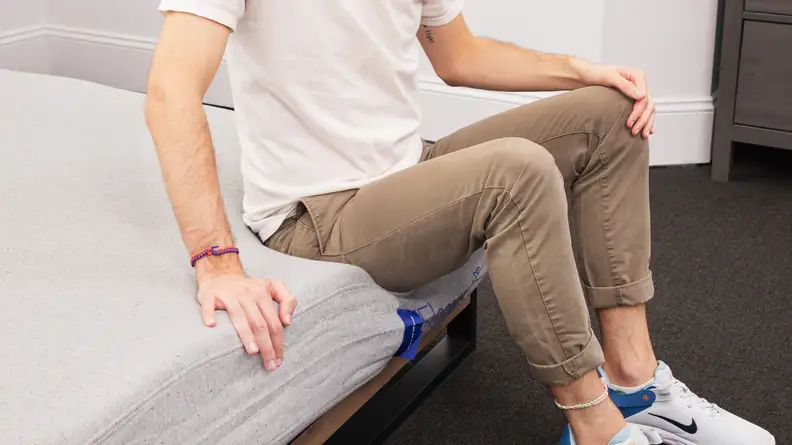 A person sitting on the edge of the mattress as the mattress itself gives out with no support.