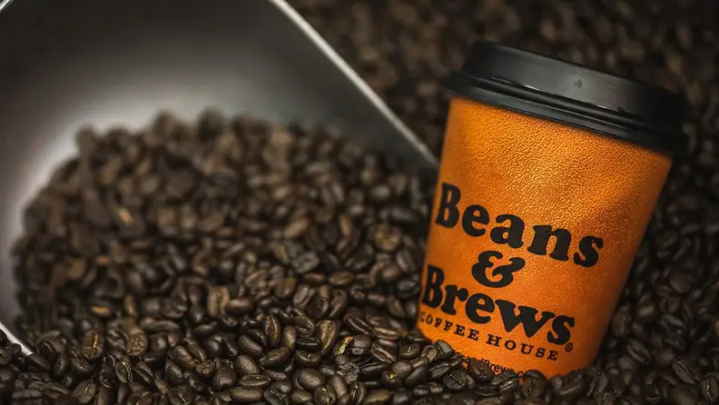 Orange Beans & Brews cup resting in a scoop of coffee beans