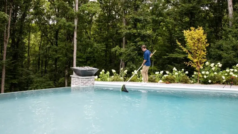 Man skimming leaves from an infinity pool with a net