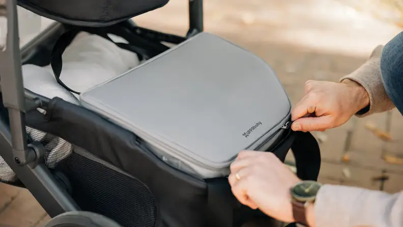 Close-up image of a parent's hands as they push their child in a stroller equipped with the UppaBaby Bevvy cooler.