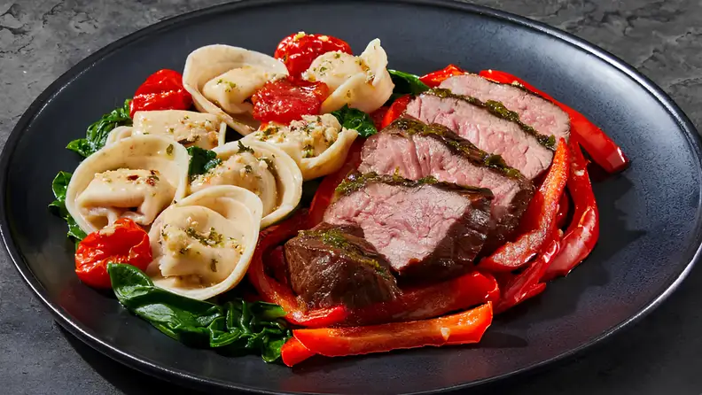 Prepared meal for one person featuring sliced steak, tortellini, and vegetables plated as a balanced single-serving dish.