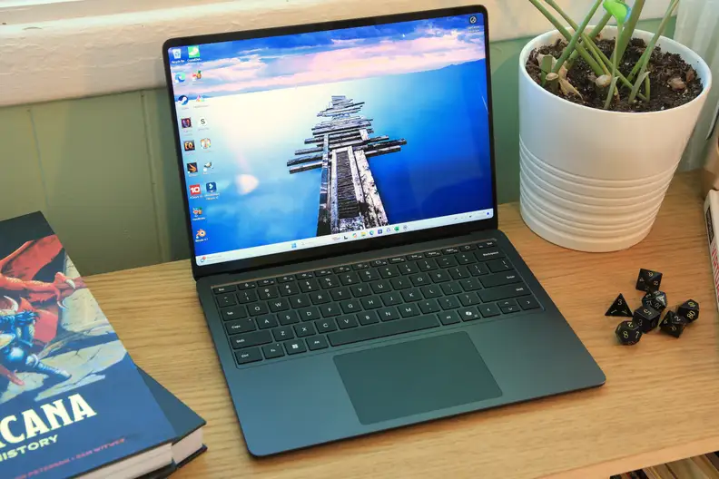The Microsoft Surface 7th Gen. laptop sitting on a desk next to a potted plant and a stack of books.