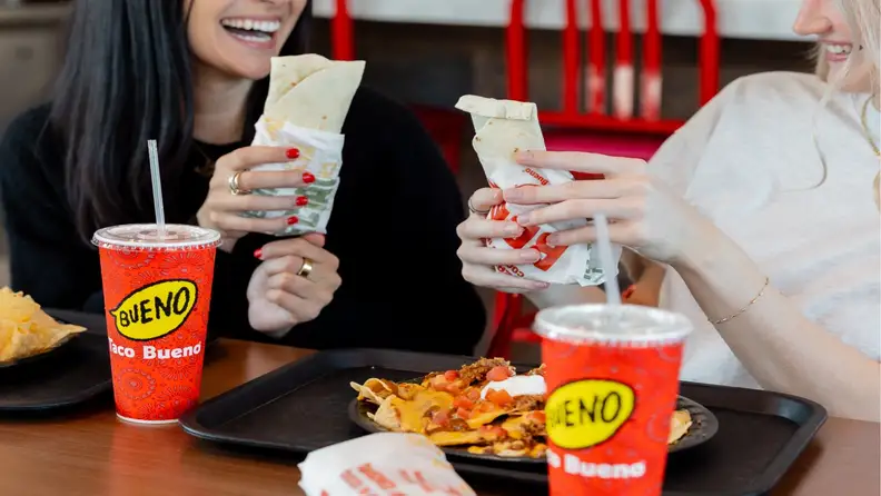 Two women holding burritos at a table with nachos and drinks