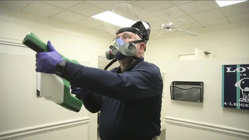 Technician wearing respirator mask spraying pesticide indoors
