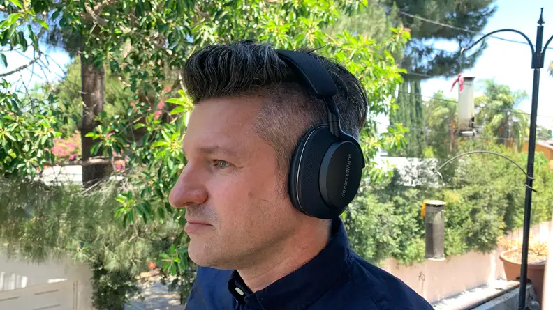 A man stands on a balcony listening to music while wearing the Bowers & Wilkins Px7 S2 headphones.
