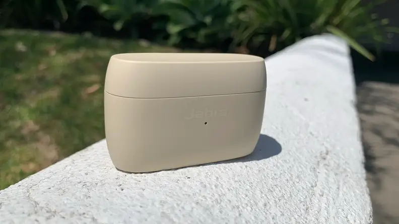 The gold beige charging case for the Jabra Elite 5 sits on a white stone wall.