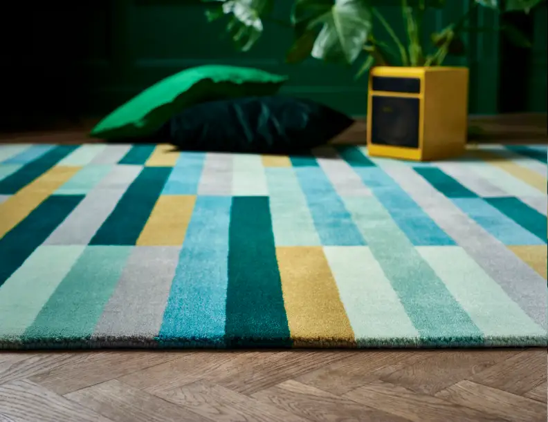 The Krônge rug's color palette includes green, teal, gray, and yellow