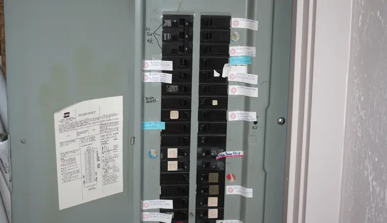 A standard green electrical panel stands open with all a home's circuits inside