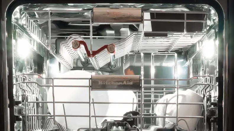 A close-up of the KitchenAid KDPM804KBS dishwasher with the door open, showing the two LEDs illuminating the interior. They're located about halfway into the device, along the left and right top edges.