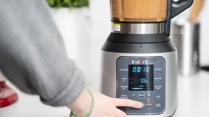 A person pushes a button to set the speed on a blender filled with soup.