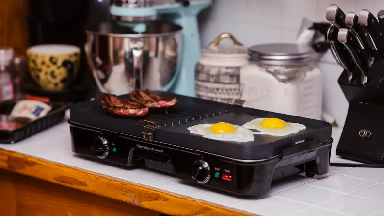 Griddle with bacon and eggs cooking on counter
