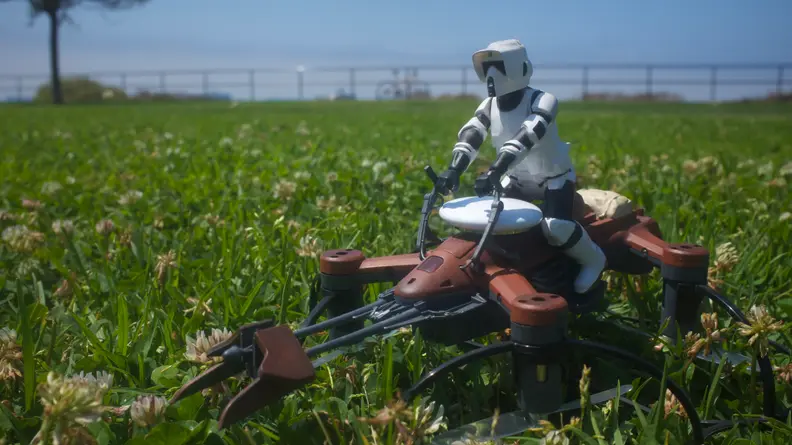 An Apple AirTag resting atop a Star Wars drone, sitting in the park.
