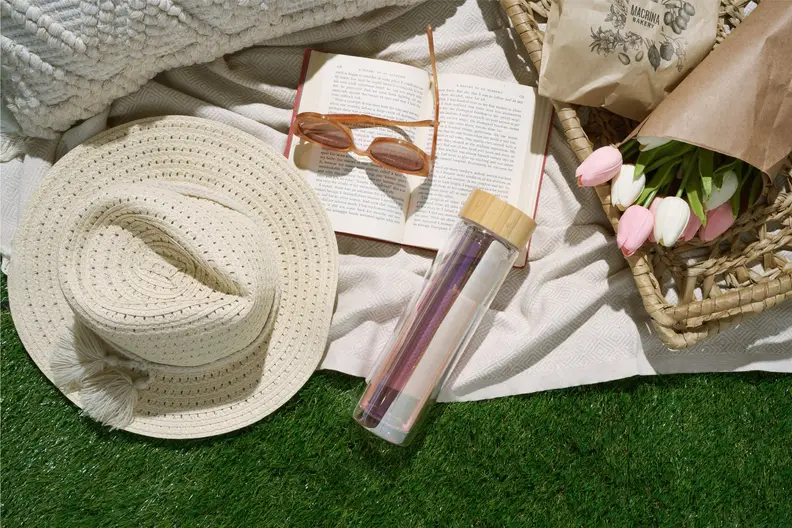 travel mug next to hat, glasses, and bag on grass