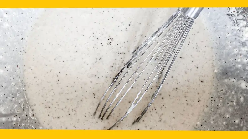 A whisk leans against the side of a bowl filled with waffle batter.