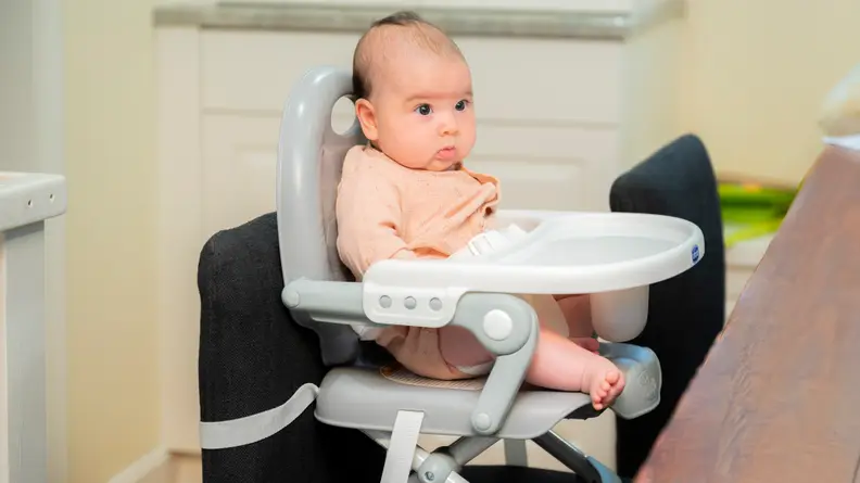 A baby sitting in a booster seat at a dining table.