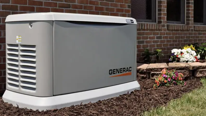 A standby generator made by Generac, sitting against the outside wall of a home.