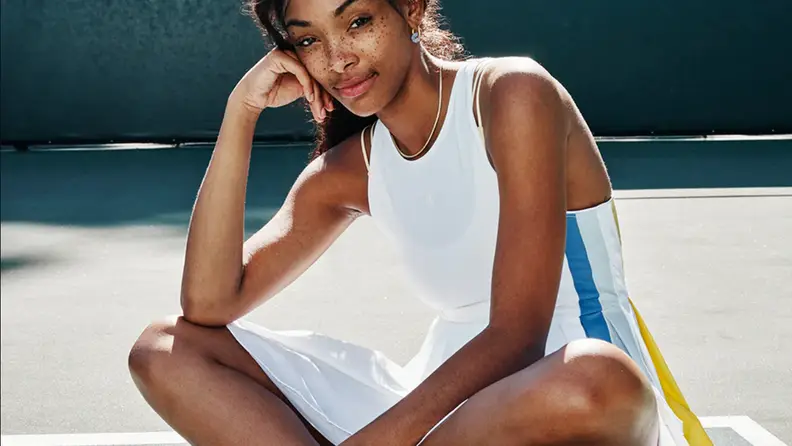 Woman wearing tennis dress sitting on court