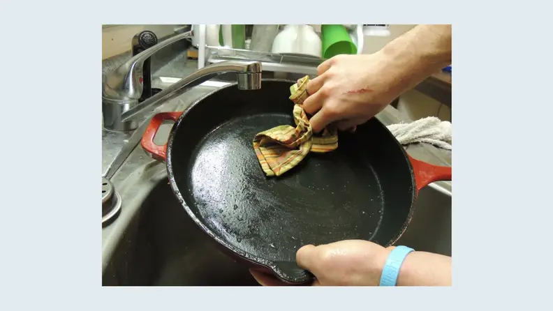 Une personne essuie une poêle en fonte avec un chiffon.