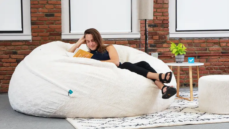 A woman comfortable on a Lovesac bean bag while she reads a book.