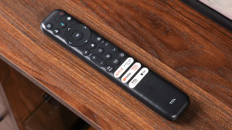 TCL Q6 LED TV remote sitting on top of wooden TV stand.
