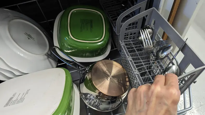 A close-up of a hand reaching into frame to tilt the cutlery basket towards the viewer.