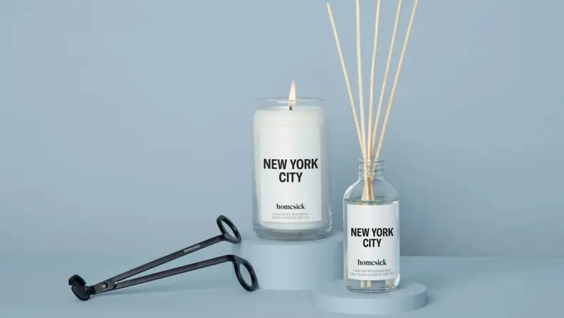 Scent diffuser and burning candle in front of blue background.