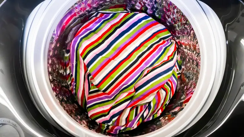 A shot of the Samsung WA50R5400AV top-loading washing machine's interior drum.  At the bottom of the drum, for scale and as a pop of color, is a rainbow beach towel.